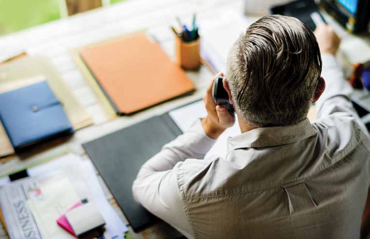 Gestor fala ao telefone em uma mesa com pastas e documentos