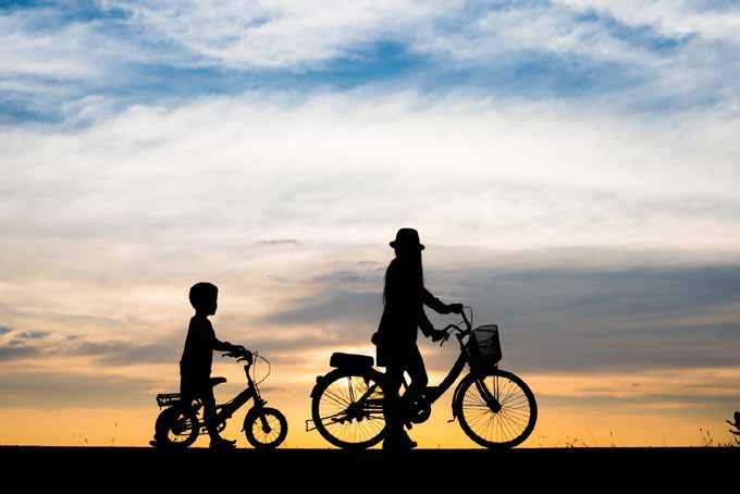 Adulto e criança caminham com bicicletas ao pôr do sol